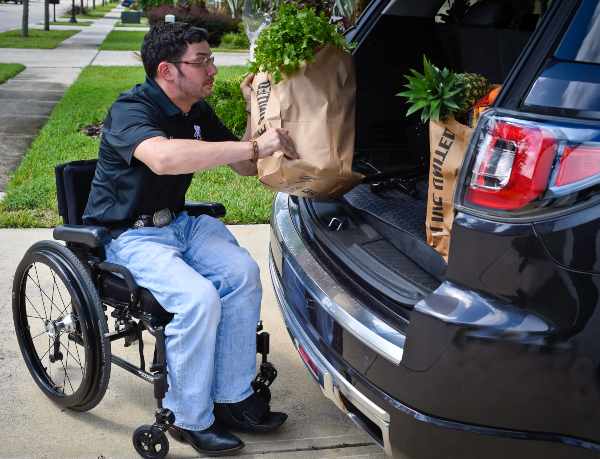 wounded warrior unloading groceries from back of car in a wheelchair